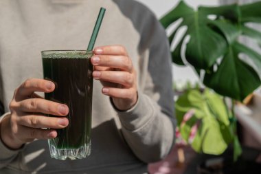 Tarafsız bej arka planda doğal organik yeşil spirulina alg tozu içen tanınmamış bir kadın. Chlorella deniz yosunu vejetaryen süper yemek kokteylleri smoothie takviye kaynağı ve detoks içeceği.
