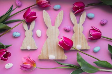 Paskalya yumurtaları ve pembe laleli ahşap tavşanlar menekşe pastel arka planda. Düz konum, üst görünüm. Dekorasyon minimalist modern tasarım şablonu. Yaratıcı ilkbahar çiçekli düzen
