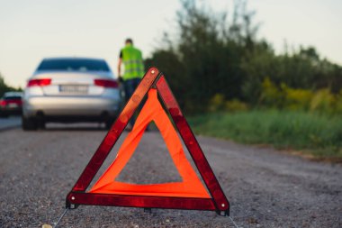 Kırık gümüş rengi lüks araba acil durum kazası. Adam sürücü yola kırmızı üçgen dur işareti yerleştiriyor. Spor otomobiller yolda sinyal lambalarını çalıştırdı. Güvenlik prosedürü