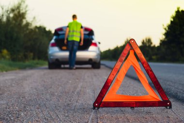 Kırık gümüş rengi lüks araba acil durum kazası. Adam sürücü yola kırmızı üçgen dur işareti yerleştiriyor. Spor otomobiller yolda sinyal lambalarını çalıştırdı. Güvenlik prosedürü