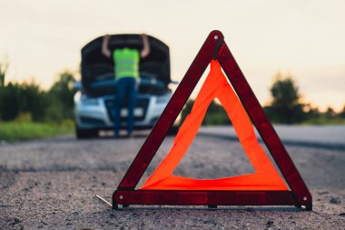 Kırık gümüş rengi lüks araba acil durum kazası. Adam sürücü yola kırmızı üçgen dur işareti yerleştiriyor. Spor otomobiller yolda sinyal lambalarını çalıştırdı. Güvenlik prosedürü