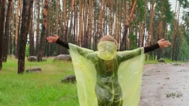 秋の森を歩く黄色いレインコートの笑顔の女性は 雨天を屋外で楽しんでいます 女性観光客が雨季に公園を発見 自然に近づいている メンタルヒーリングフルフィルメントクリーンエアー — ストック動画