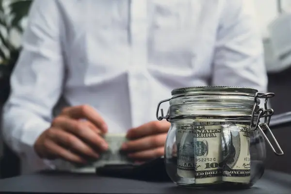 Dollar Banknote Saving Money In Glass Jar. Unrecognizable man calculate money on calculator Moderate Consumption And Economy Collecting Money Tips Business Finance concept