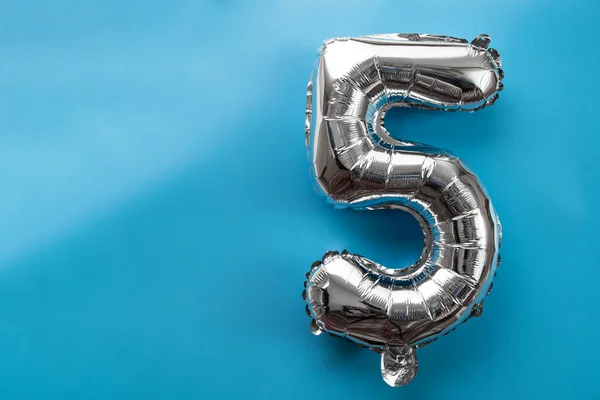 5 five metallic balloon isolated on blue background. Greeting card silver foil balloon number Happy birthday holiday concept. Copy space for text. Celebration party congratulation decoration
