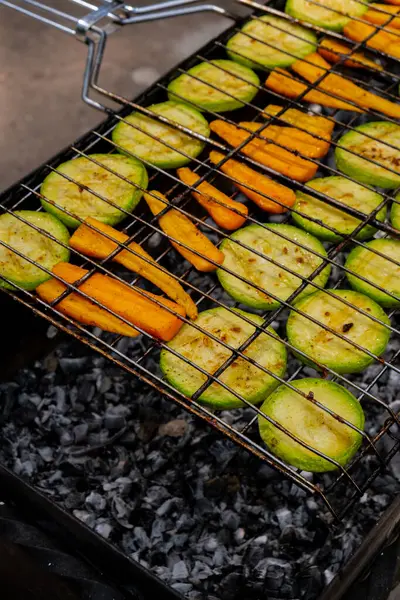 Chopped zucchini and carrots roasting on fire seasoned with aroma herbs and spices. Delicious fresh vegetables grilling on barbecue smoker grid. Diet vegan bbq. Outdoor recreation in backyard