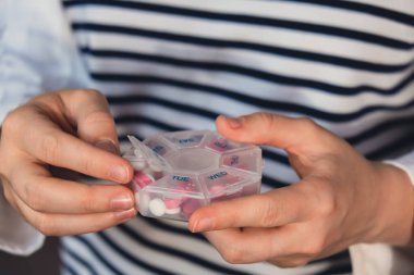 Woman sorting pills Organizer weekly shots Closeup of medical pill box with doses of tablets for daily take medicine with white pink drugs and capsules. Young woman getting her daily vitamins at home