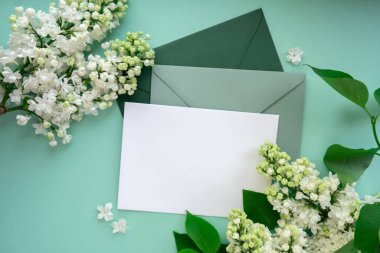 Boş yeşil zarflı kompozisyon ve nane arkaplanda güzel bahar leylak çiçekleri. Mockup kart davetiyesi tebrik kartı posta kartı kopyalama alanı şablonu boş. Çiçek açan leylak dalları