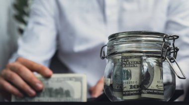 Dolar banknotu cam kavanozda para biriktiriyor. Tanınmayan adam, Orta Yol Tüketim ve Ekonomi Biriktirme İşletme Finansmanı kavramında para hesapladı