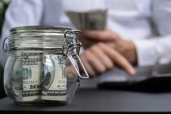 Dollar Banknote Saving Money In Glass Jar. Unrecognizable man calculate money on calculator Moderate Consumption And Economy Collecting Money Tips Business Finance concept