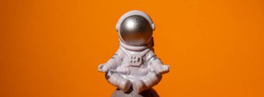 Plastic toy astronaut on colorful orange background Copy space. Concept of out of earth travel, private spaceman commercial flights. Space missions and Sustainability