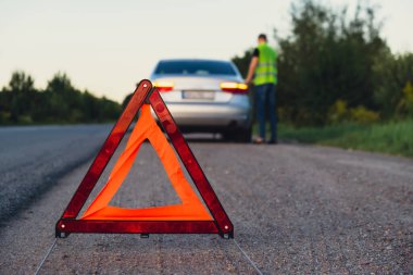 Kırık gümüş rengi lüks araba acil durum kazası. Adam sürücü yola kırmızı üçgen dur işareti yerleştiriyor. Spor otomobiller yolda sinyal lambalarını çalıştırdı. Güvenlik prosedürü
