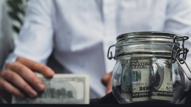 Adam hesap makinesinde masraf banknotlarını sayıyor. Tanınmayan bir iş adamının eli kulağında. Bütçe yatırımı kavramını sakla. Amerikan doları tasarruf fonu kavramı