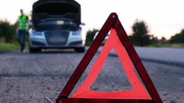 Kırık gümüş rengi lüks araba acil durum kazası. Adam sürücü yola kırmızı üçgen dur işareti yerleştiriyor. Spor otomobiller yolda sinyal lambalarını çalıştırdı. Güvenlik prosedürü