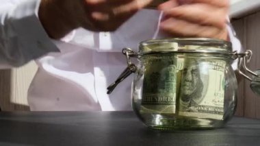 Adam kumbaradaki cam kavanozdan gelen dolar banknotlarını sayıp sayıyor. Tanınmayan bir iş adamının eli kulağında. Bütçe yatırımı kavramını sakla. Amerikan doları.
