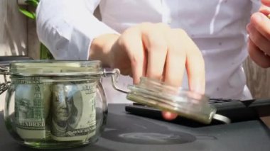Adam kumbaradaki cam kavanozdan gelen dolar banknotlarını sayıyor ve hesap makinesinde sayıyor. Tanınmayan bir iş adamının eli kulağında. Bütçe yatırım kavramını sakla