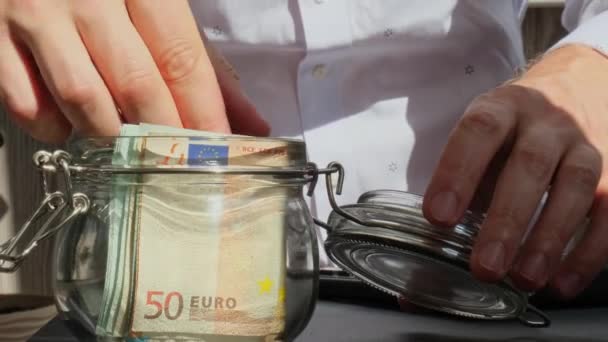 人工在计算器上从储蓄罐的玻璃罐子里数着欧元现金的费用钞票 不明不白的商人缩手缩脚 节约预算投资的概念 欧元基金节余 — 图库视频影像