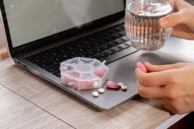 Günlük vitaminler alan beyaz bir kadın dizüstü bilgisayar organizatörü haftalık olarak tıbbi hap kutusunu ilaçlarla kapatıyordu. Günlük dozlarda beyaz pembe haplar ve kapsüllerle ilaç alıyordu. İş yeri ilaçları diyet takviyeleri, dokunulmazlık ve hastalık tanıtımı