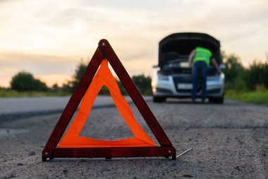 Kırık gümüş rengi lüks araba acil durum kazası. Adam sürücü yola kırmızı üçgen dur işareti yerleştiriyor. Spor otomobiller yolda sinyal lambalarını çalıştırdı. Güvenlik prosedürü