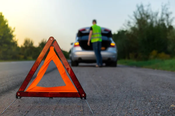 Kırık gümüş rengi lüks araba acil durum kazası. Adam sürücü yola kırmızı üçgen dur işareti yerleştiriyor. Spor otomobiller yolda sinyal lambalarını çalıştırdı. Güvenlik prosedürü