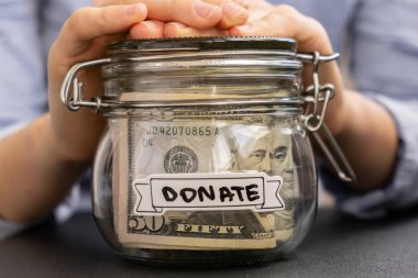 Amerikan dolarlarıyla dolu cam kavanozu elinde tutan tanınmamış bir kadın nakit para ile DONATE mesajı. Hazırlık para tasarrufu. Orta karar tüketim ve ekonomi. Para toplama