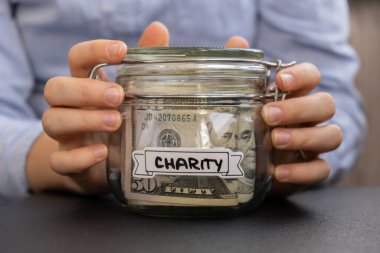 Dolar banknotlarıyla dolu cam kavanozda para biriktiren kadın elleri. Kavanozun önünde CHARITY kopyası. Gelecekteki güvensizlik geçmişi için kişisel finansman yöneticiliği