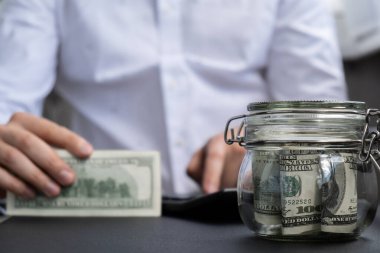 Dolar banknotu cam kavanozda para biriktiriyor. Tanınmayan adam, Orta Yol Tüketim ve Ekonomi Biriktirme İşletme Finansmanı kavramında para hesapladı
