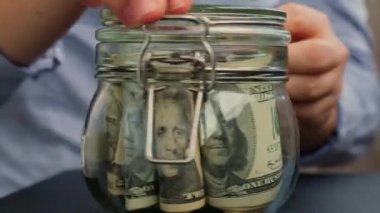 Tanınmayan bir kadın para biriktirme kavanozunu dolar banknotlarıyla doldurdu. Morgage transkripti kavanozun önünde. Gelecekteki güvensizlik geçmişi için kişisel finansman yöneticiliği