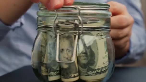 无法辨认的女人把钱藏在装有美元钞票的玻璃瓶里 Mortgage转录在罐子前 为今后的不安全背景管理个人财政额外收入 — 图库视频影像