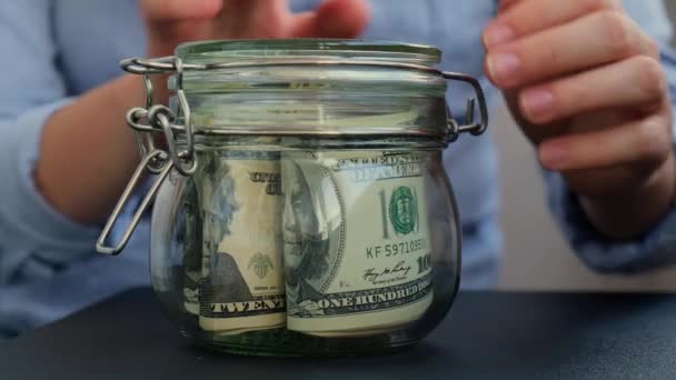 女性手存钱转玻璃瓶装满美元钞票 Tips转录在罐子前面为今后的不安全背景管理个人财政额外收入 — 图库视频影像