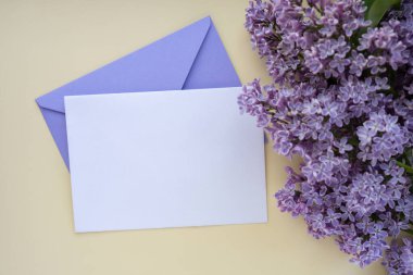 Boş menekşe zarflı kompozisyon ve bej arka planda güzel bahar leylak çiçekleri. Mockup kart davetiyesi tebrik kartı posta kartı kopyalama alanı şablonu boş. Çiçek açan leylak dalları