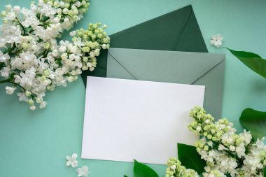 Boş yeşil zarflı kompozisyon ve nane arkaplanda güzel bahar leylak çiçekleri. Mockup kart davetiyesi tebrik kartı posta kartı kopyalama alanı şablonu boş. Çiçek açan leylak dalları