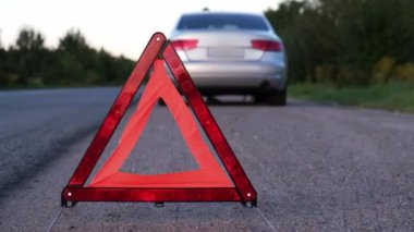 Kırık gümüş rengi lüks araba acil durum kazası. Adam sürücü yola kırmızı üçgen dur işareti yerleştiriyor. Spor otomobiller yolda sinyal lambalarını çalıştırdı. Güvenlik prosedürü