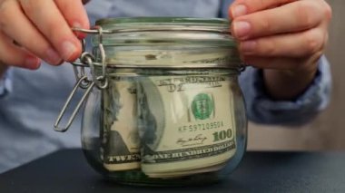 Tanınmayan bir kadın para biriktirme kavanozunu dolar banknotlarıyla doldurdu. Kavanozun önünde ev metni var. Gelecekteki güvensizlik geçmişi için kişisel finansman yöneticiliği