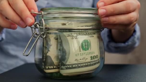 无法辨认的女人把钱藏在装有美元钞票的玻璃瓶里 家里转录在罐子前面 为今后的不安全背景管理个人财政额外收入 — 图库视频影像
