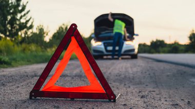 Kırık gümüş rengi lüks araba acil durum kazası. Adam sürücü yola kırmızı üçgen dur işareti yerleştiriyor. Spor otomobiller yolda sinyal lambalarını çalıştırdı. Güvenlik prosedürü