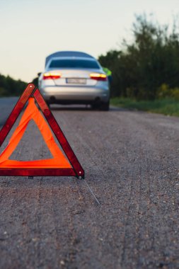 Kırık gümüş rengi lüks araba acil durum kazası. Adam sürücü yola kırmızı üçgen dur işareti yerleştiriyor. Spor otomobiller yolda sinyal lambalarını çalıştırdı. Güvenlik prosedürü