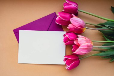 Bej arka planda güzel pembe lale buketi olan metin ya da tasarımın için boş beyaz zarf kopyalama alanı. Tatil bahar tebrik kartı için şablon oluşturun. Üst görünüm Düz boş kağıt kadın yatıyordu