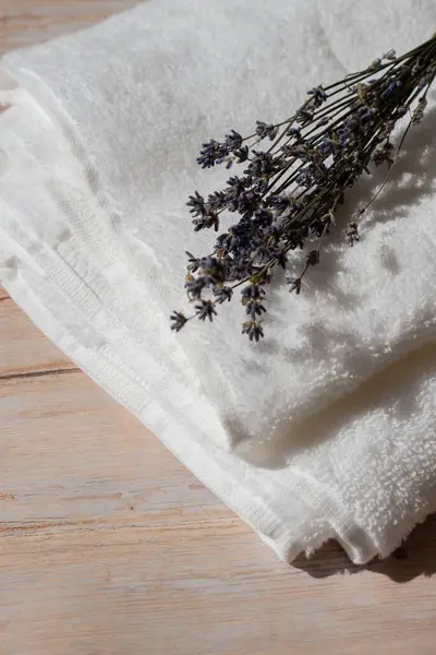 Lavender flowers next to white cotton towel on wooden background. Aromatherapy and organic concept. Still life of dried lavender herbs. Eco sustainable concept