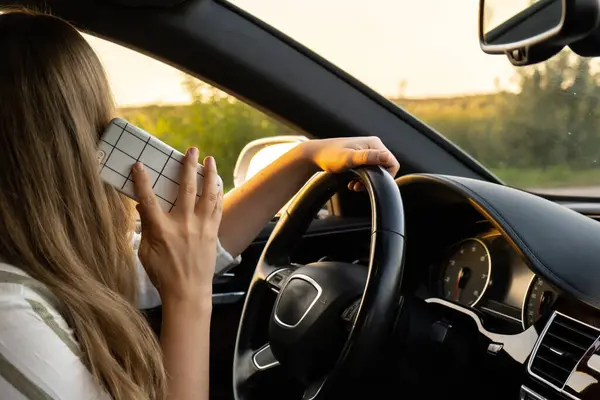 Happy young woman speaking by mobile phone while driving car. Business woman talking phone call in automobile. Unsafely risky driving. Concept of multitasking