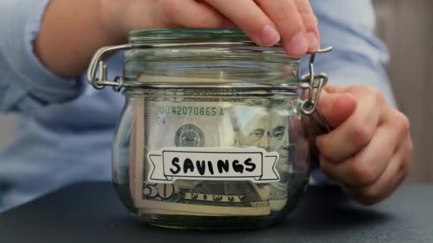 女性的手从装有美元钞票的玻璃瓶中取出钱 Donate转录在罐子前为今后的不安全背景管理个人财政额外收入 — 图库视频影像