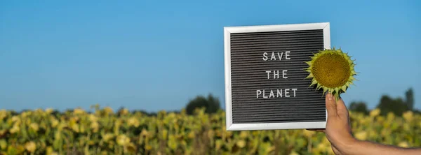 Unrecognizable person with banner message SAVE THE PLANET in sunflower field on sunny day. Sign EARTH day. Concept of ecology and eco activism environmental issues Stop global warming. Go green sustainable