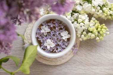 Lezzetli siyah çay beyaz bardakta pencere kenarında aromatik leylak çiçekleriyle. Bahar kompozisyonu bir bardak leylak çayı içerken mor leylak dalları çiçek açıyor. Kopya uzay tebrik kartı, poster, afiş, duvar kağıdı için hala hayat var. Rahatlama ve doğal