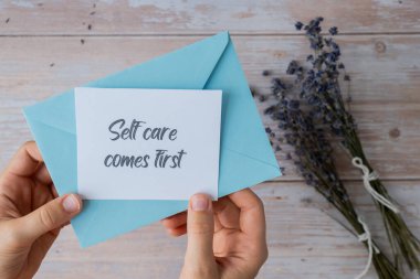 Dişi eller, mavi zarftan ilk olarak SELF CARE yazılı kâğıt kağıdı alıyor. Lavanta çiçeği. Üst manzara, düz yatış. Ruhsal sağlık hizmeti kavramı, farkındalıktır.