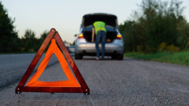 Kırık gümüş rengi lüks araba acil durum kazası. Adam sürücü yola kırmızı üçgen dur işareti yerleştiriyor. Spor otomobiller yolda sinyal lambalarını çalıştırdı. Araç bozulduğunda güvenlik prosedürü