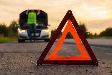 Kırık gümüş rengi lüks araba acil durum kazası. Adam sürücü yola kırmızı üçgen dur işareti yerleştiriyor. Spor otomobiller yolda sinyal lambalarını çalıştırdı. Araç bozulduğunda güvenlik prosedürü