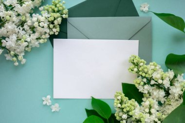 Boş yeşil zarflı kompozisyon ve nane arkaplanda güzel bahar leylak çiçekleri. Mockup kart davetiyesi tebrik kartı posta kartı kopyalama alanı şablonu boş. Çiçek açan leylak dalları. 