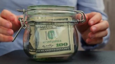 Tanınmayan bir kadın para biriktirme kavanozunu dolar banknotlarıyla doldurdu. Kavanozun önünde INSURANCE transkripti. Gelecekteki güvensizlik geçmişi için kişisel finansman yöneticiliği