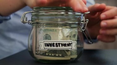 Tanınmayan bir kadın, içi dolar banknotlarıyla dolu Cam Kavanozda Para Kurtarma 'dan para alıyor. Kavanozun önüne transkripsiyon. Gelecekteki güvensizlik için kişisel finansman yöneticiliği