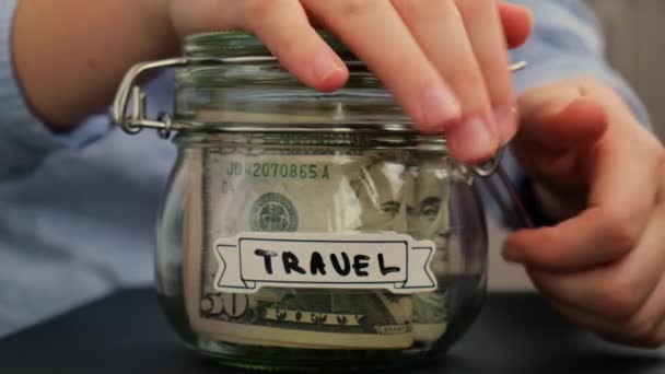 女性の手は テキストTravelでアメリカの通貨ドル紙幣でいっぱいのガラス瓶からお金を取ります お金を節約する準備 適度な消費と経済 お金の収集について — ストック動画