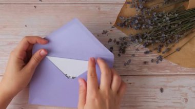 Kadın eller, menekşe zarfından POSİF HAYAT VİBESİ yazılı kâğıt not alıyor. Lavanta çiçeği. Üst manzara, düz yatış. Ruhsal sağlık hizmeti kavramı, farkındalıktır.